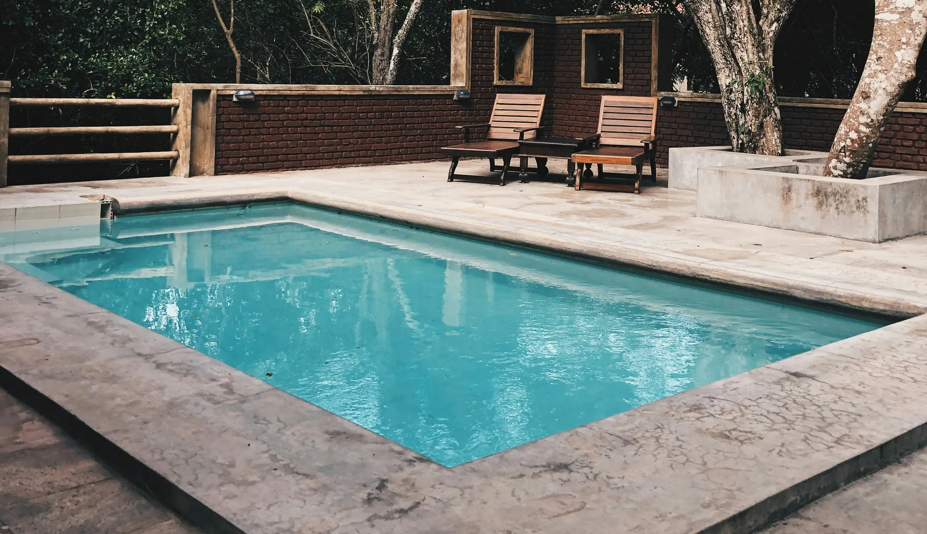 Outdoor pool with wooden lounge chairs and trees